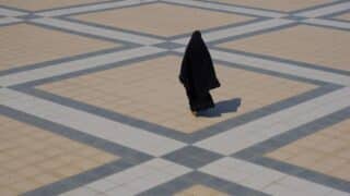 woman in black walking on beige and gray tiled surface with geometric pattern and shadow.