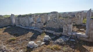 Ancient stone ruins with standing walls and columns in a grassy area under a clear sky.