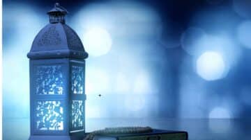 Decorative lantern, floral patterns, soft blue light, near prayer beads and book, blurred background.