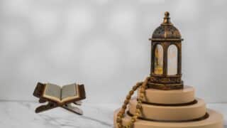 Traditional lantern, wooden platforms, prayer beads, open book on stand, serene setting.