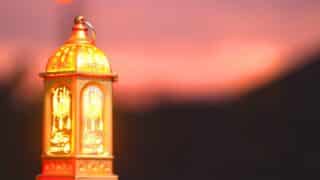 Decorative lantern with intricate designs lit against a warm sunset background.