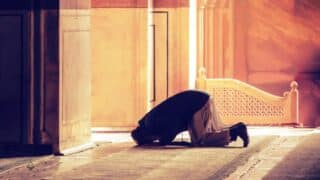 Person kneeling in prayer in a warmly lit room with ornate architectural details and patterns.