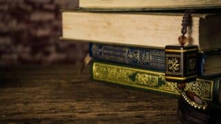 Close-up of three ornate books with Arabic script and tassel on wooden surface.