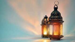 Two lit metal lanterns with intricate patterns, casting a warm glow on a blurred background.