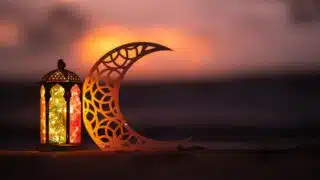 Decorative lantern with colorful glass beside crescent cutout at sunset, warm ambiance.