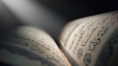 Quran book with Arabic script illuminated by soft light beam.