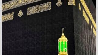 Close-up of the Kaaba with black covering, gold calligraphy, and green lantern on marble.