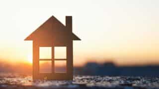 Wooden house cutout against sunrise or sunset, sun illuminating its interior.