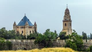 Historical complex with octagonal building, blue roof, clock tower, stone wall, and greenery.