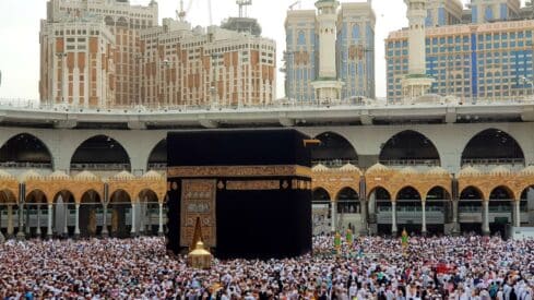 Kaaba in Mecca with pilgrims and modern buildings in Masjid al-Haram.