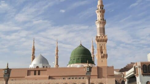 prophet Mosque with green dome, minarets, and beige stonework against a partly cloudy sky.