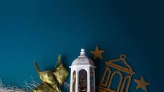 Decorative white lantern with gold stars, frame, green ornament, and string on teal background.