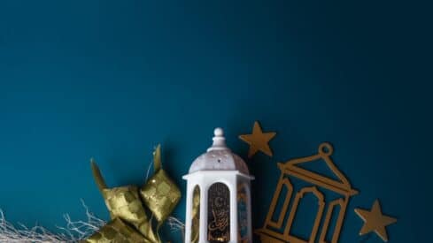 Decorative white lantern with gold stars, frame, green ornament, and string on teal background.