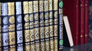 Ornate books with gold patterns and Arabic script on a shelf, part of a numbered series.