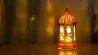 Ornate lantern with patterns and warm glow on wooden surface, softly lit background.