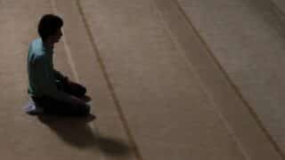 Person kneeling on striped carpet, hands on knees, creating a shadow in dim lighting.