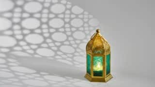 Decorative lantern with golden frame and teal glass casting patterned shadows on a light surface.