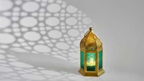 Decorative lantern with golden frame and teal glass casting patterned shadows on a light surface.