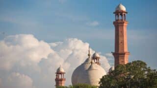 Mosque with a central dome and two minarets, cloudy sky, greenery.