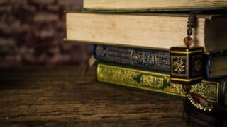 Stack of ornate books with decorative covers and a beaded tassel on a wooden surface.