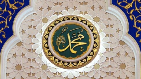 Circular medallion with word of mohammed, gold border, green center, floral pattern background.