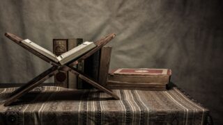 Wooden desk with office supplies, quran, and writing tools on polished hardwood floor in still life composition