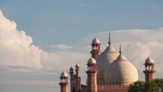 Historic mosque with large domes and minarets against a blue sky with fluffy clouds. The architectural details feature intricate carvings and a symmetrical design, showcasing traditional styles. Ideal for cultural and travel-related content.