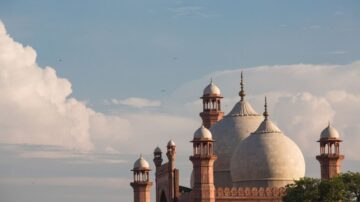 Historic mosque with large domes and minarets against a blue sky with fluffy clouds. The architectural details feature intricate carvings and a symmetrical design, showcasing traditional styles. Ideal for cultural and travel-related content.